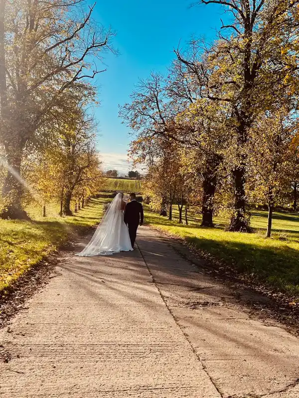 Newlyweds walking along the tree-lined drive at Thief Hall