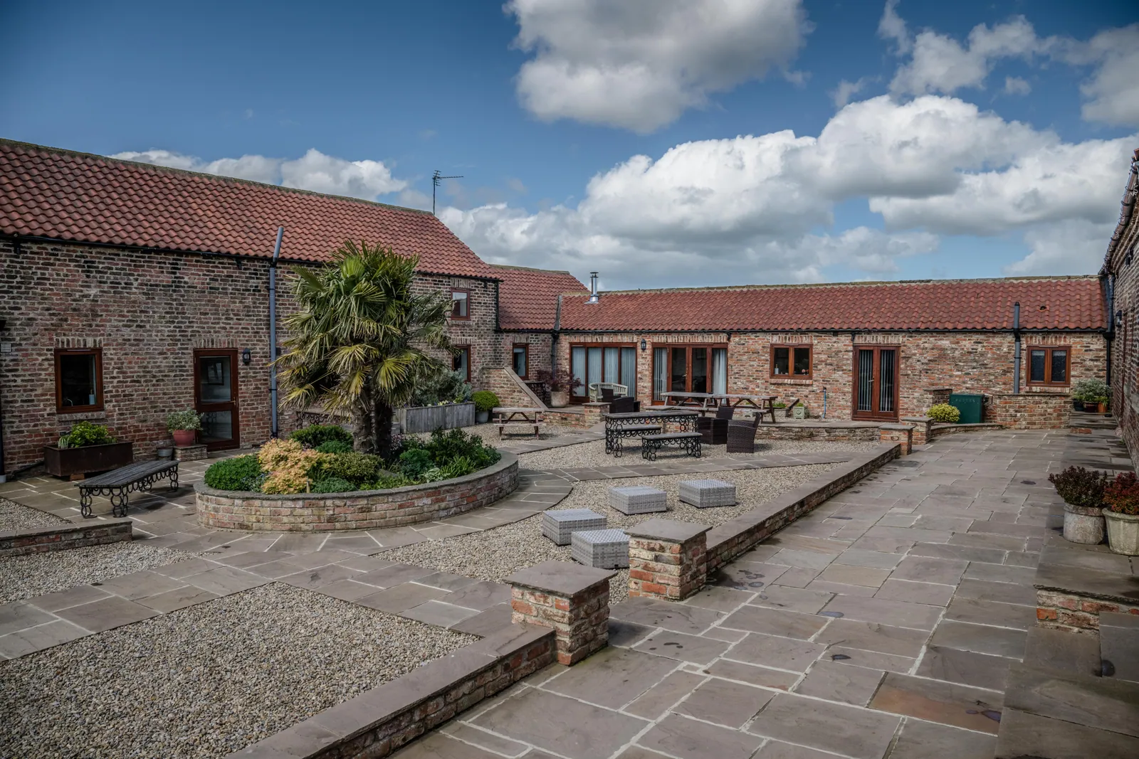 An enclosed courtyard of brick and stone barn ranges with red pantile roofs