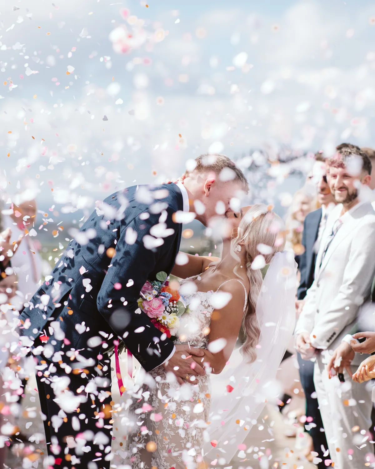 A newly married couple kissing as confetti fills the air around them