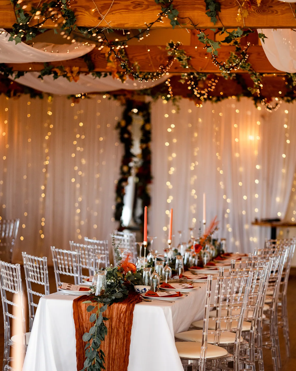 A wedding breakfast table beneath draped fabric and fairy lights