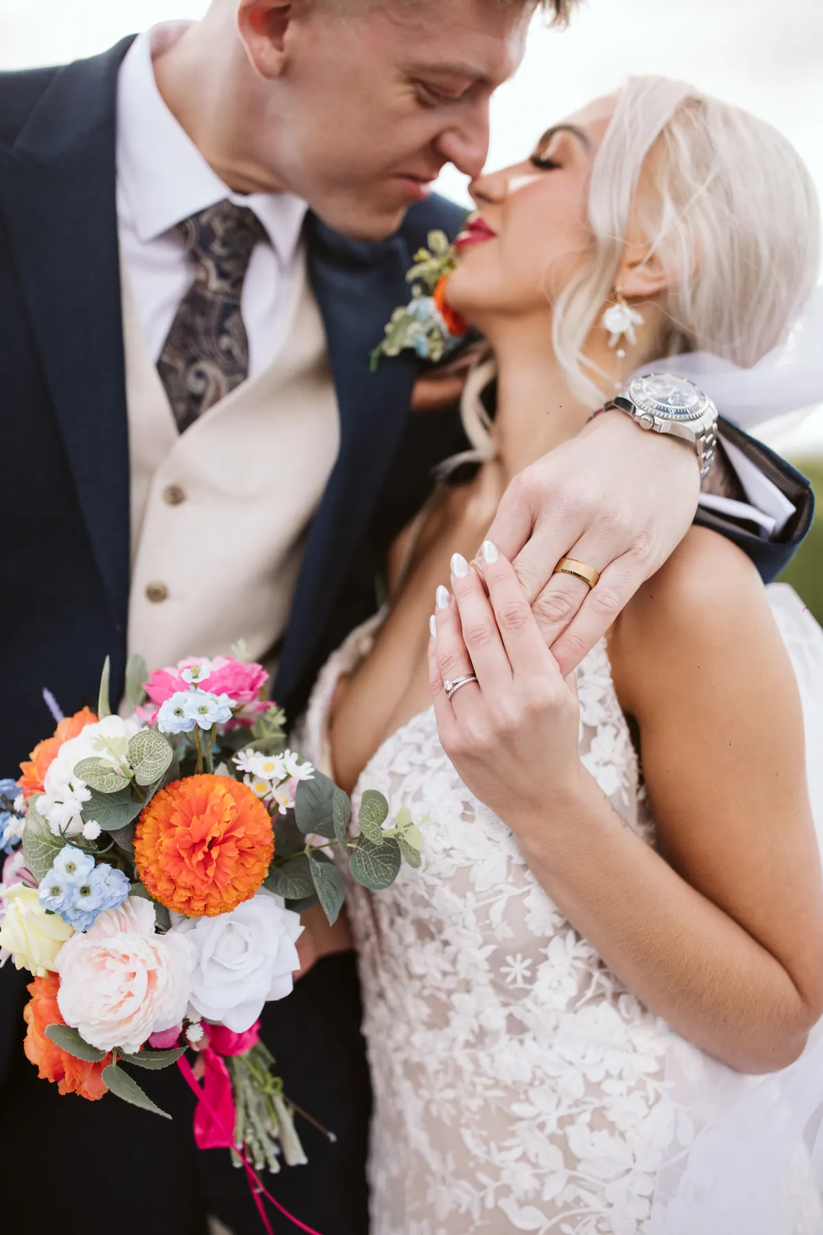 A newlywed couple holding hands beside a colourful bouquet