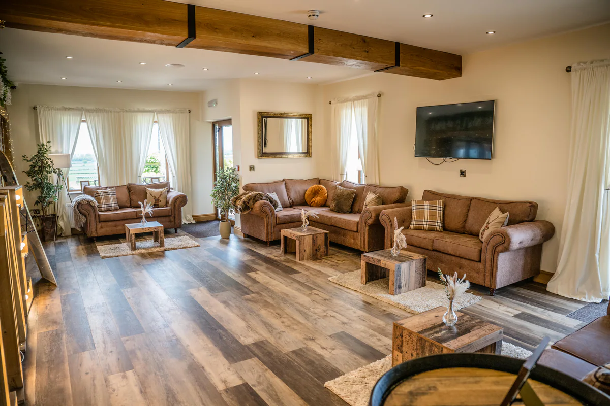 A lounge with tan leather sofas under oak beams and windows out to open fields