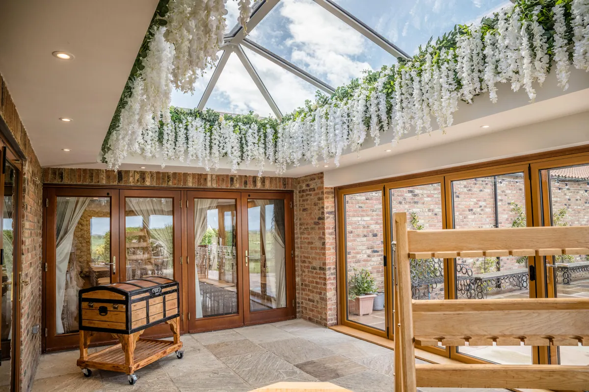 A glazed lantern roof hung with wisteria above brick and oak, with bifold doors