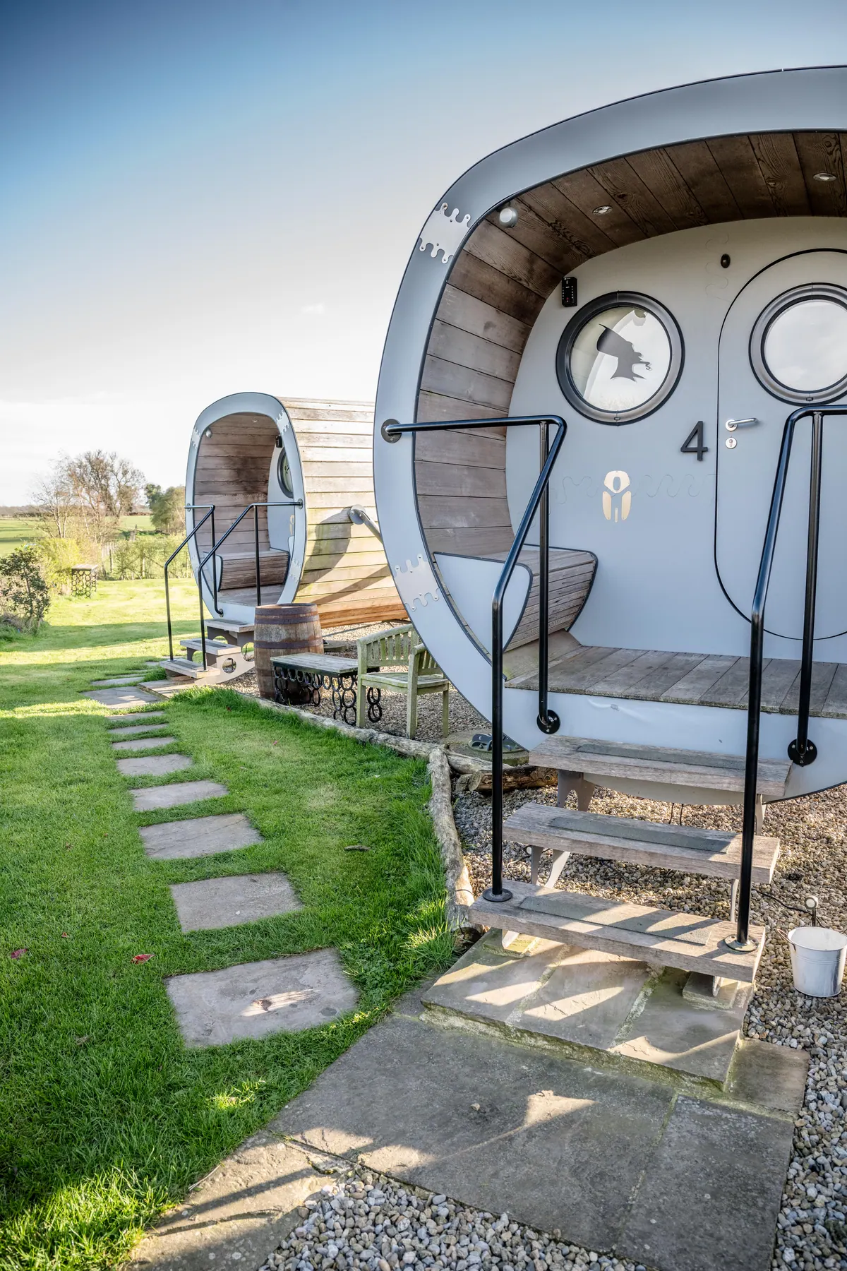 Curved timber pods with round porthole windows beside a grass path