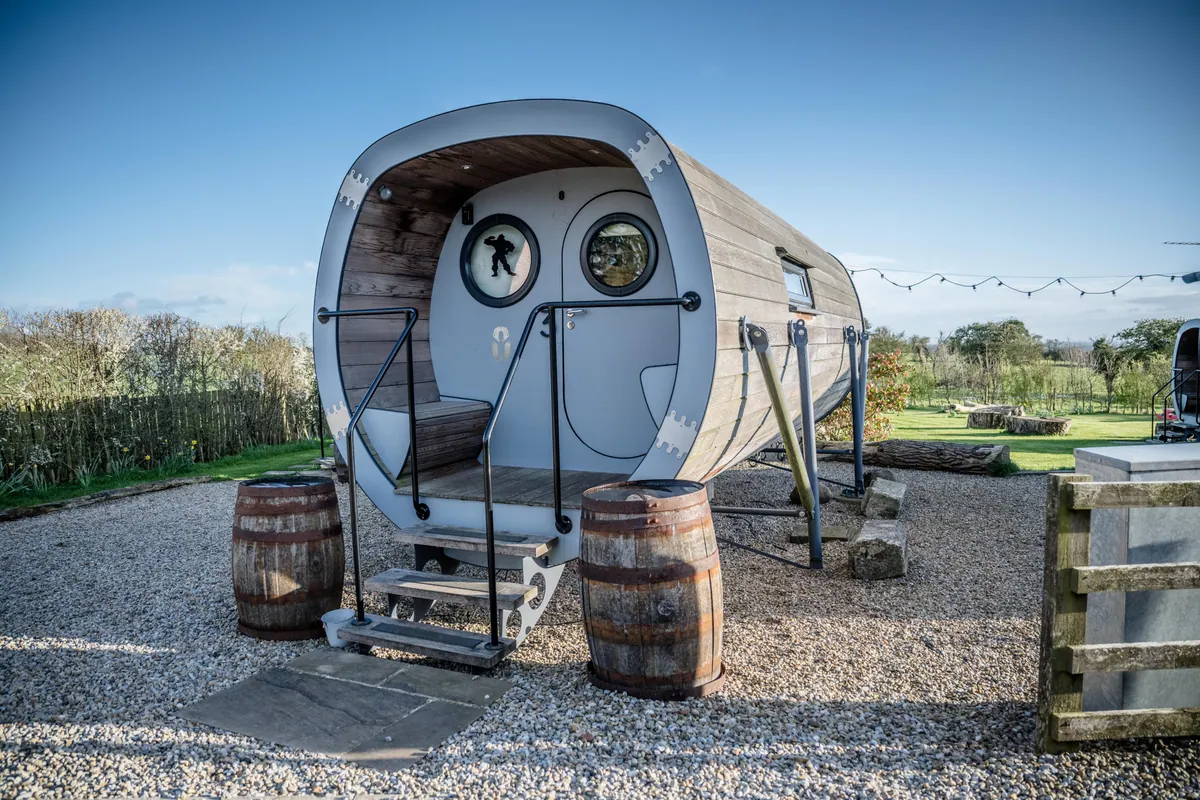 Curved timber pods with round porthole windows beside a grass path